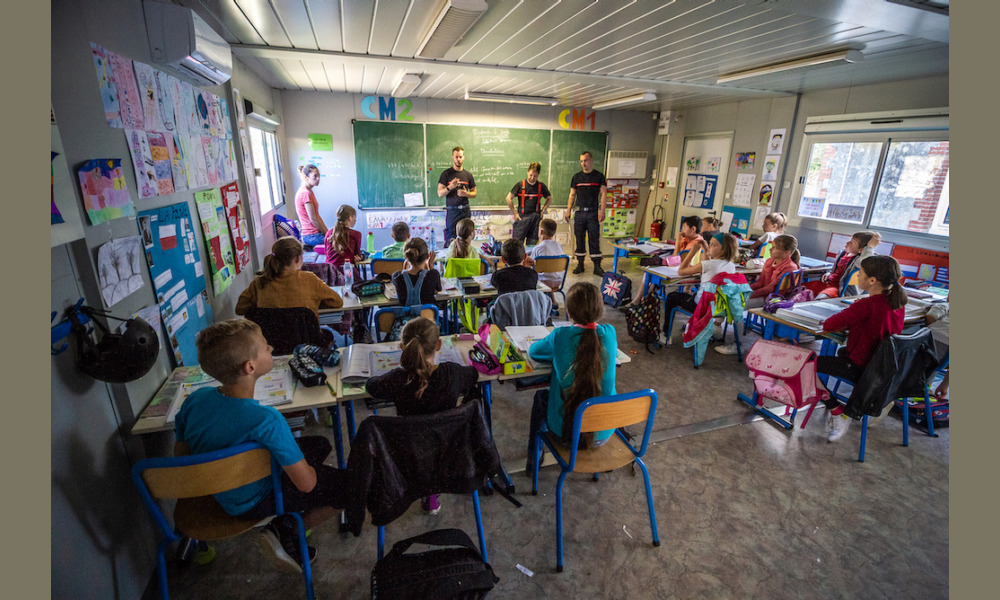 Trois pompiers volontaires échangent avec les enfants de l'école où ils viennent de finir un exercice. Certains ont besoin d'être rassurés, d'autres demandent directement la marche à suivre pour s'engager !
