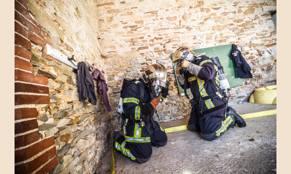 Devant la porte de la pièce où l'incendie s'est déclaré, deux pompiers volontaires ajustent une dernière fois leur tenue avant de s'attaquer au feu.