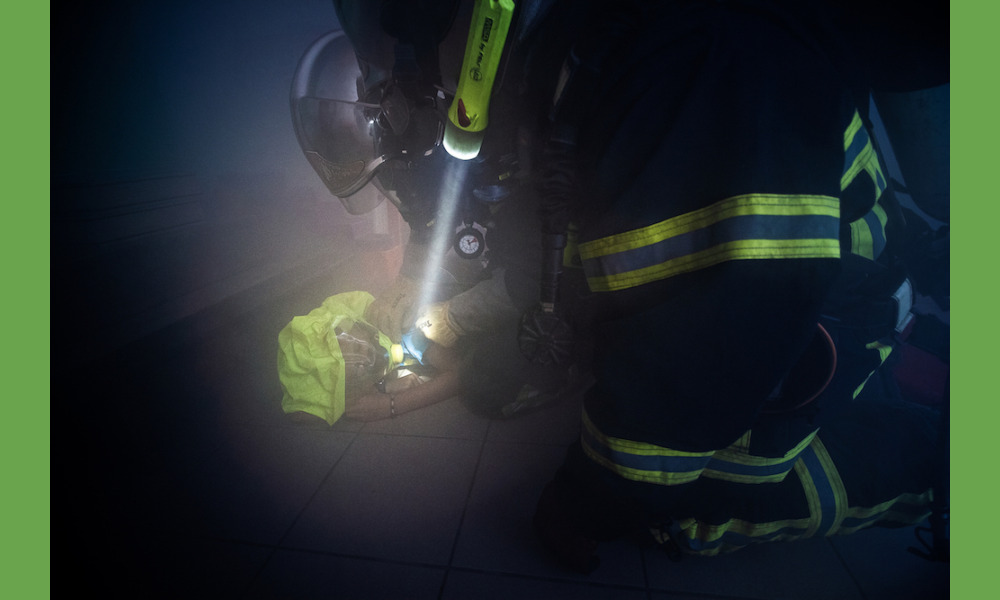À l'intérieur de la pièce, un élève joue la victime. Un masque à gaz lui est enfilé, aussi rapidement que la visibilité, quasi-nulle dans la fumée, le permet.