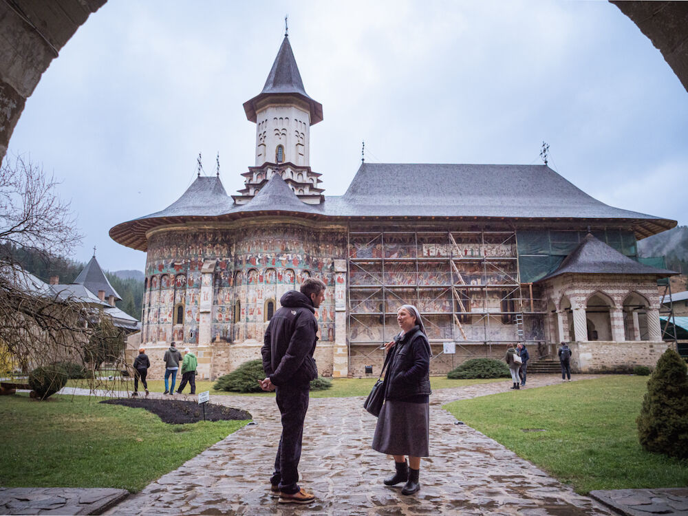 Un volontaire de Ouest-Est et Sœur Monica discutent sous la porte d'entrée du monastère de Sucevitsa, dont la fresque de l'échelle sainte, unique au monde, est en cours de rénovation.